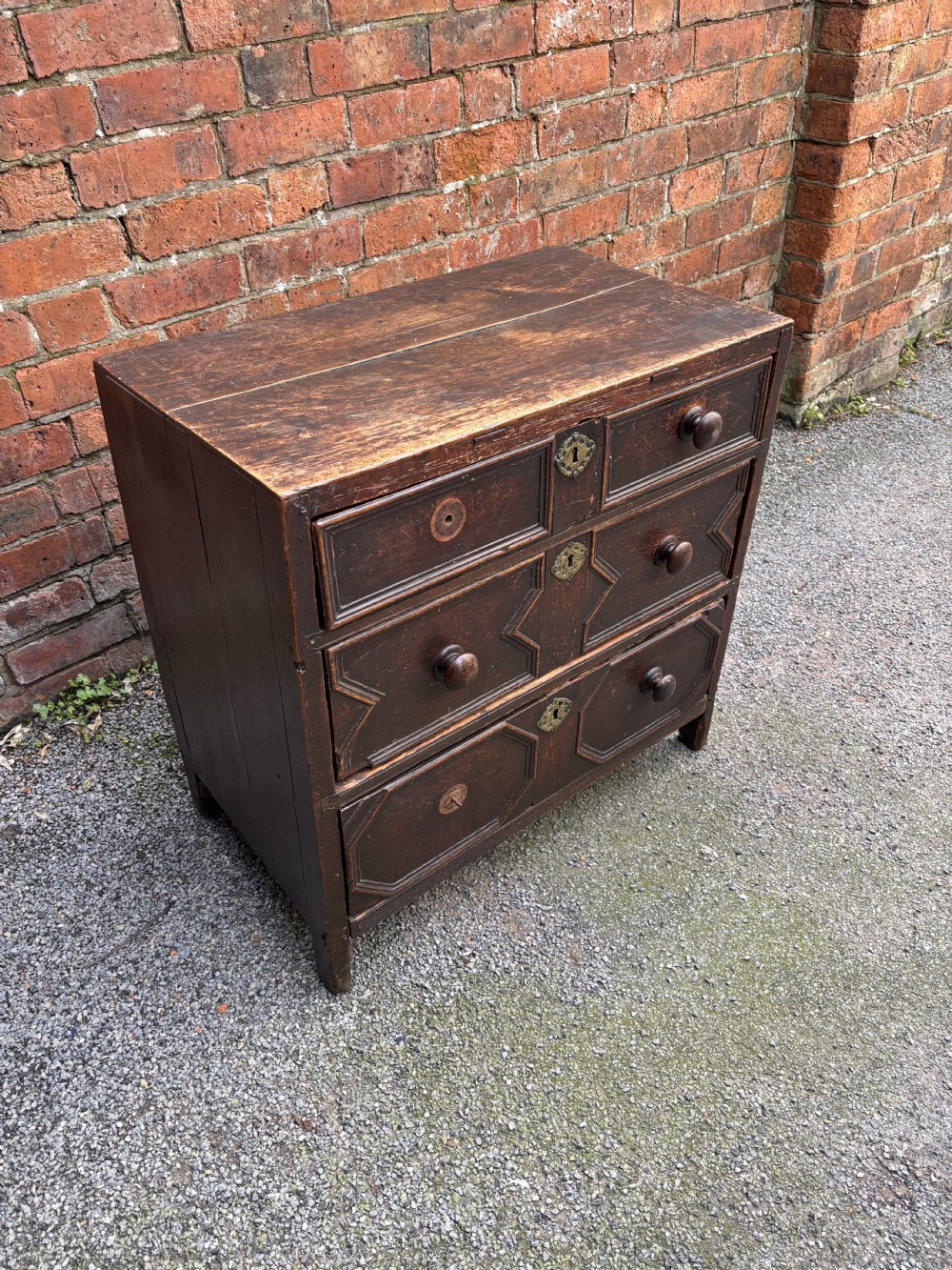 A dark oak 17th-century chest of drawers featuring geometric moulded drawer fronts, turned wooden handles, and brass escutcheons. View IV
