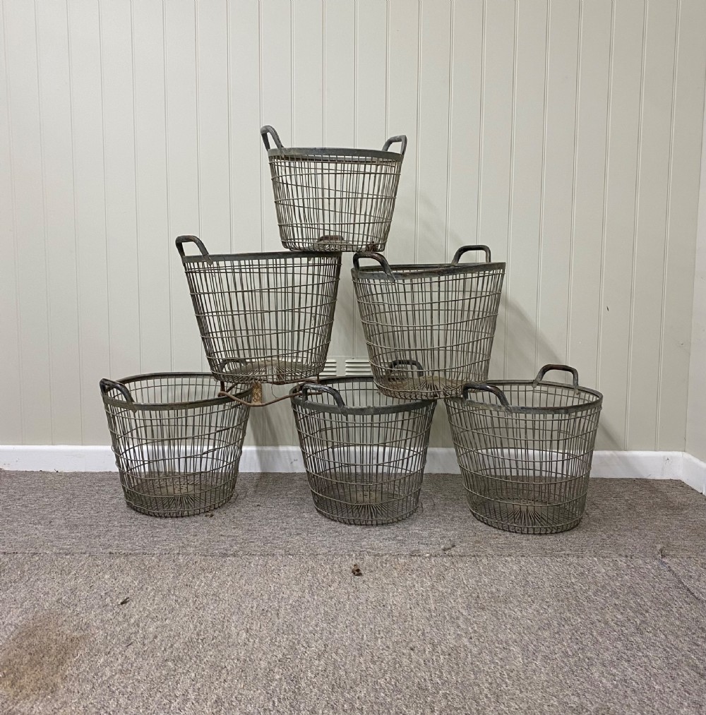 A tapered round industrial basket constructed from grey wire mesh featuring twin loop metal handles and a reinforced circular rim.