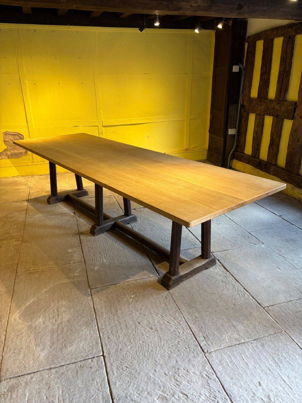 A long Arts and Crafts solid oak refectory table featuring a smooth plank top supported by a dark stained trestle base with horizontal stretchers.