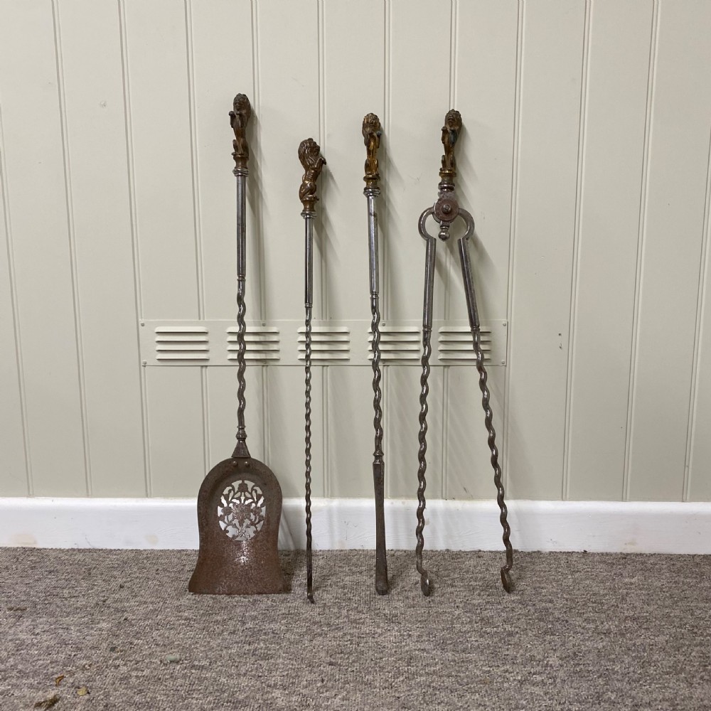 A four-piece set of antique metal fire irons featuring lion finials, barley-twist shafts, and a decorative pierced shovel.