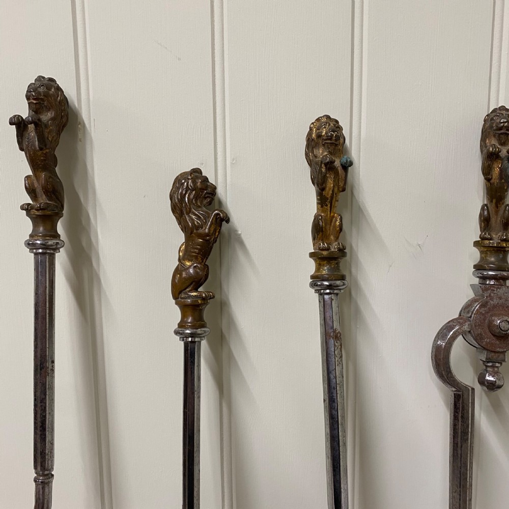 A four-piece set of antique metal fire irons featuring lion finials, barley-twist shafts, and a decorative pierced shovel. View II