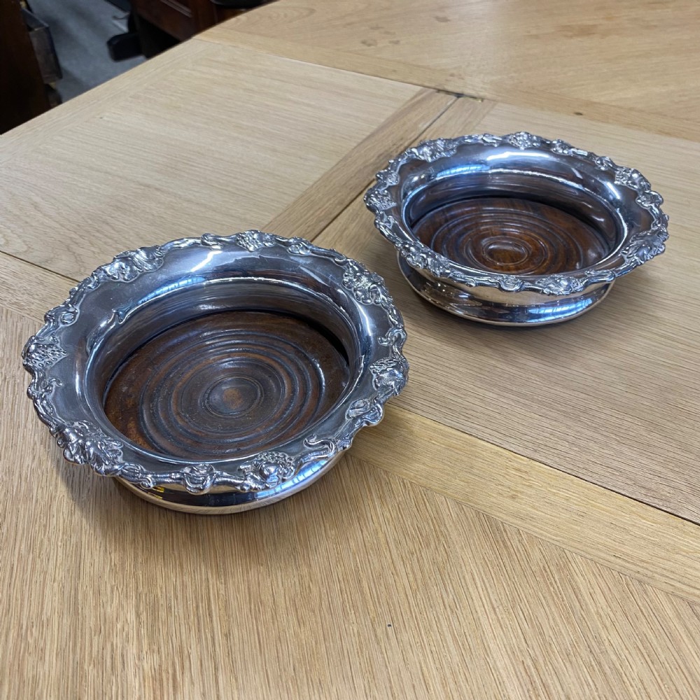 A pair of late nineteenth-century silver-plated wine coasters featuring relief grapevine borders and turned dark wood bases.