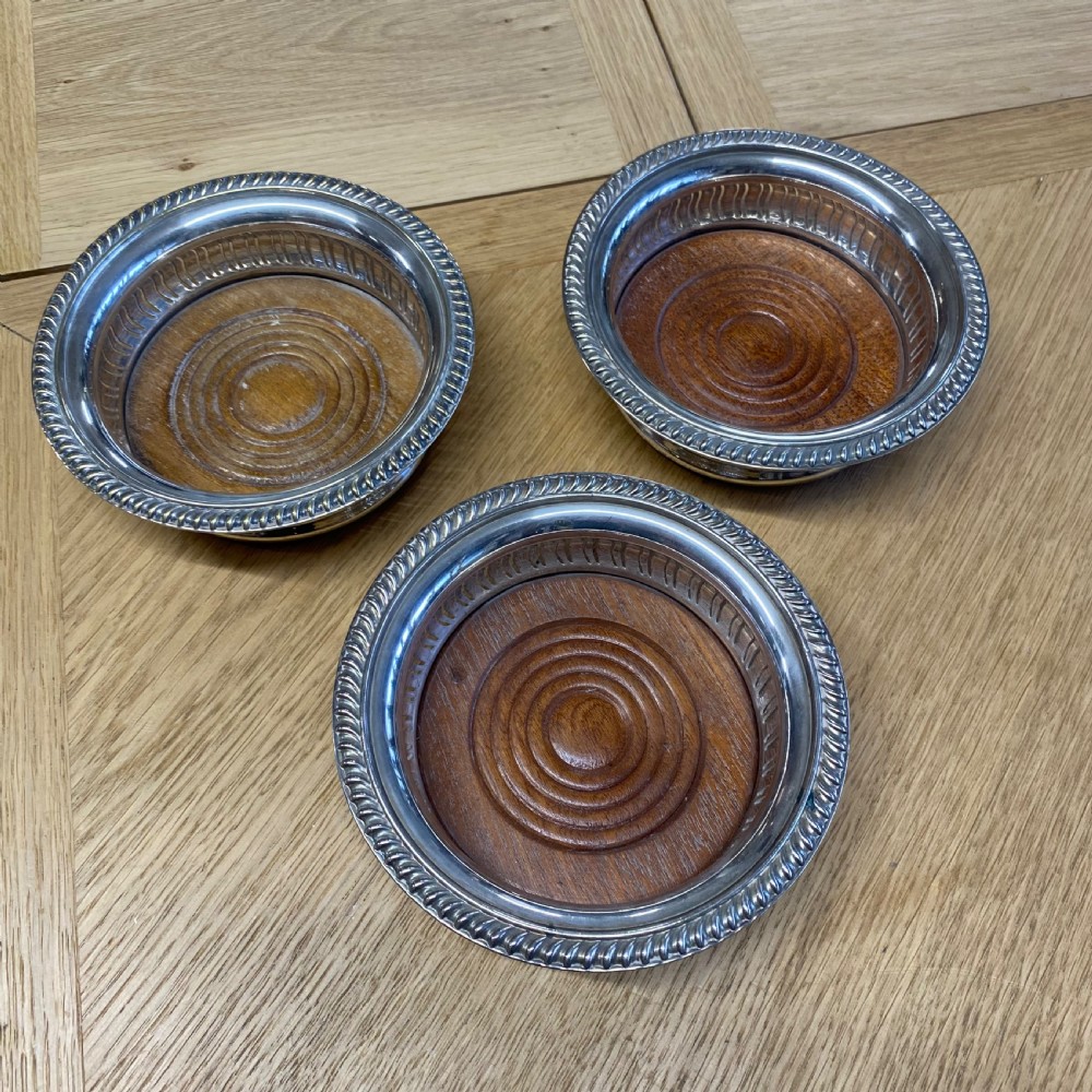 Three circular 19th-century silver-plated wine bottle coasters with turned wooden bases and rope-twist borders.
