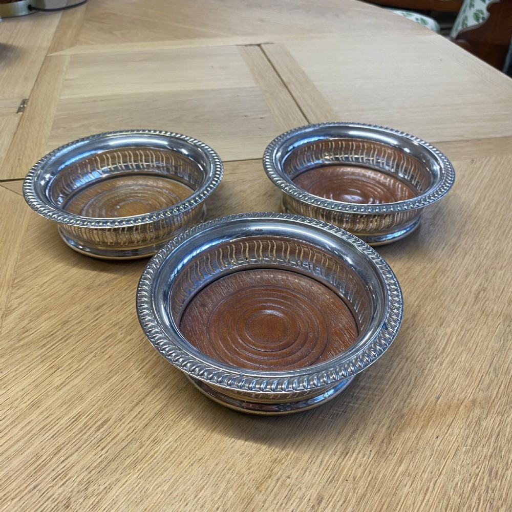 Three circular 19th-century silver-plated wine bottle coasters with turned wooden bases and rope-twist borders. View II