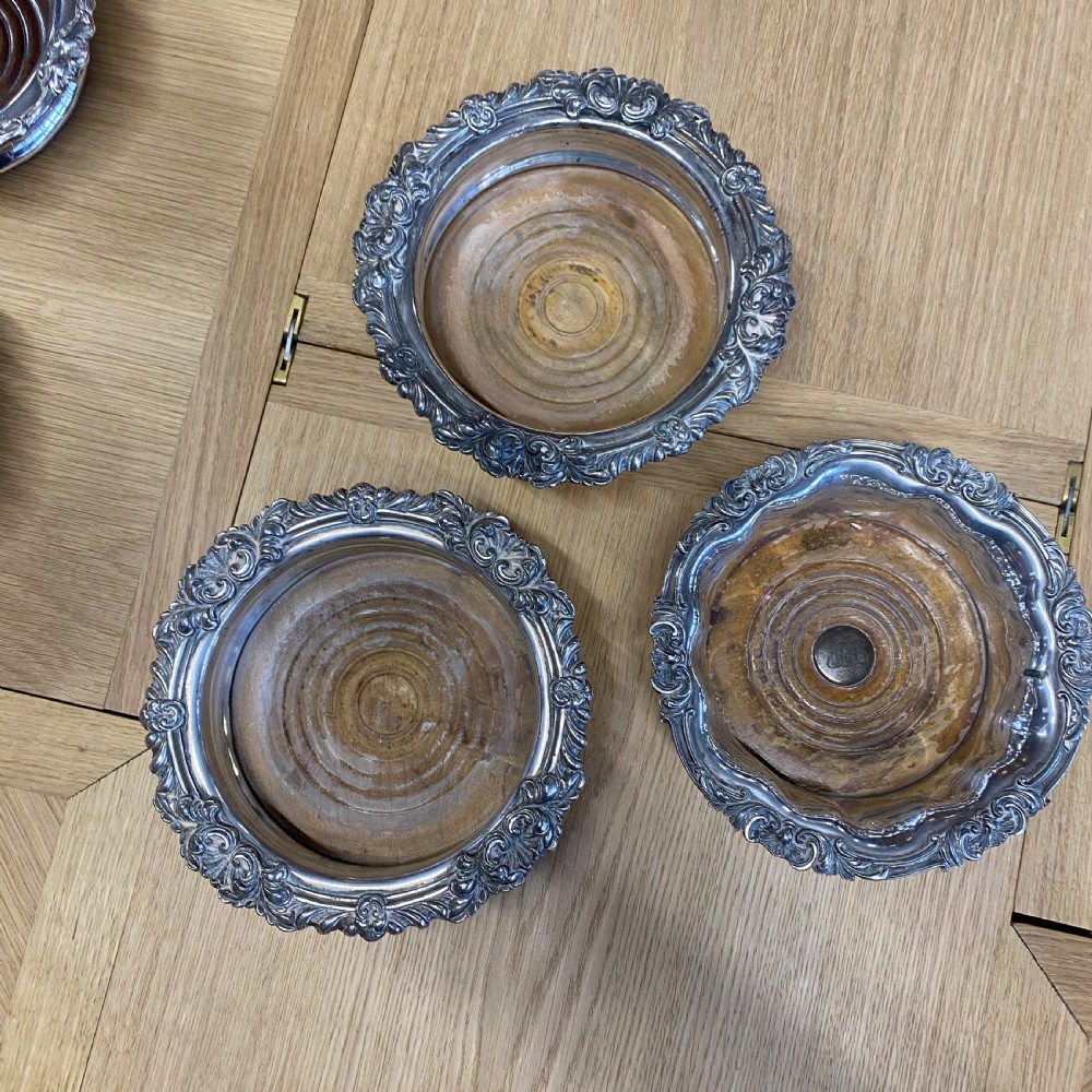 Three 19th-century silver-plated wine bottle coasters with intricate foliate rims and turned wooden bases.