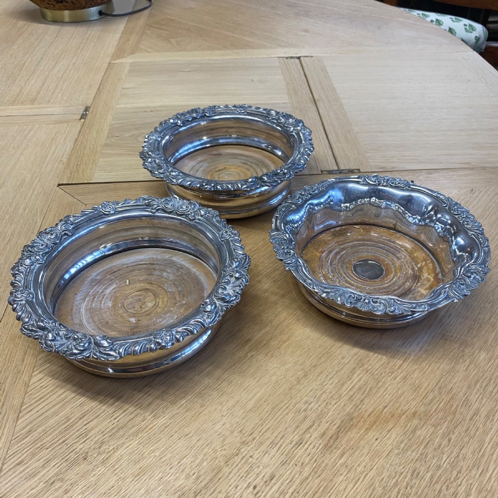 Three 19th-century silver-plated wine bottle coasters with intricate foliate rims and turned wooden bases. View II