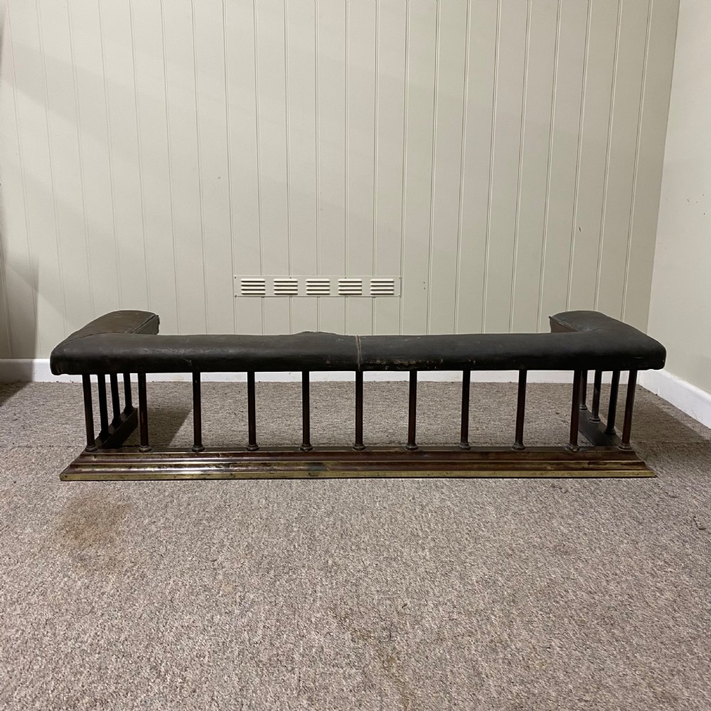 A Victorian club fender featuring a dark brown leather upholstered seat rail supported by turned wooden spindles on a polished wood and brass base.