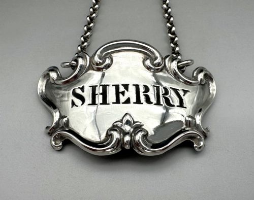 fig 1. A Victorian sterling silver decanter label with intricate scrollwork borders and a suspension chain, featuring the word SHERRY cut into the centre.