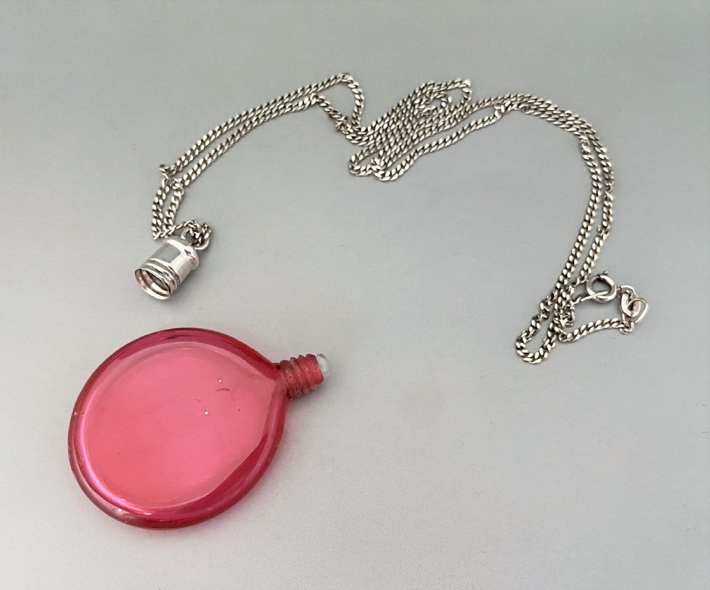 A Victorian circular cranberry glass penny scent bottle with a silver screw-top mount suspended on a fine silver chain. View IV