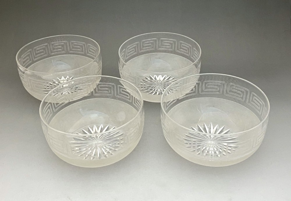 A matching set of four clear glass Victorian finger bowls featuring an etched Greek Key border pattern and a starburst cut base.