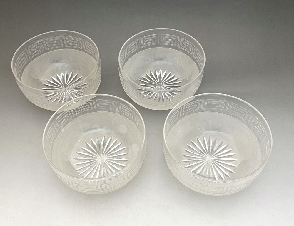 A matching set of four clear glass Victorian finger bowls featuring an etched Greek Key border pattern and a starburst cut base. View II