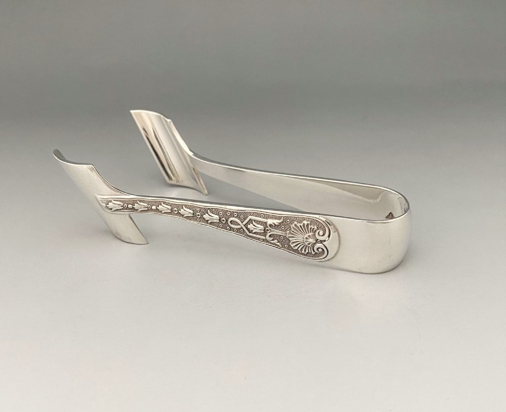 A pair of sterling silver individual asparagus tongs featuring chased shell and foliage relief work along the handles.
