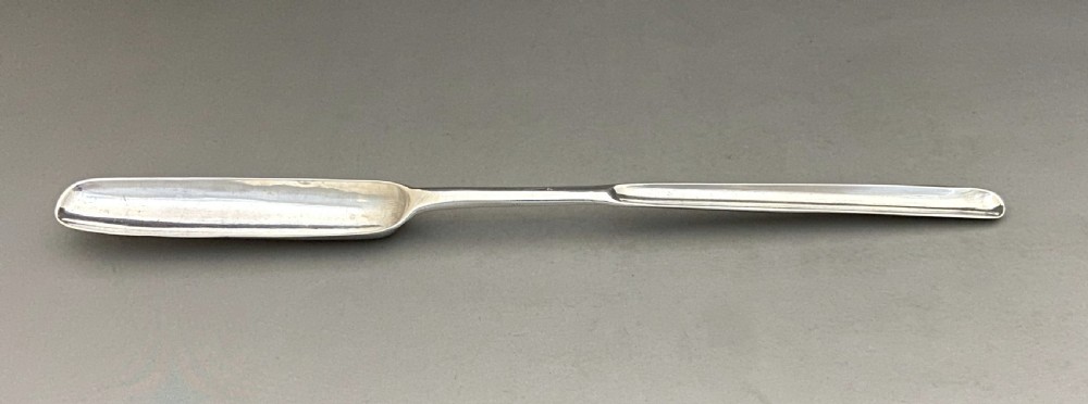 A long, slender George II sterling silver marrow scoop featuring a wide channelled scoop at one end and a narrower trough at the opposite end.
