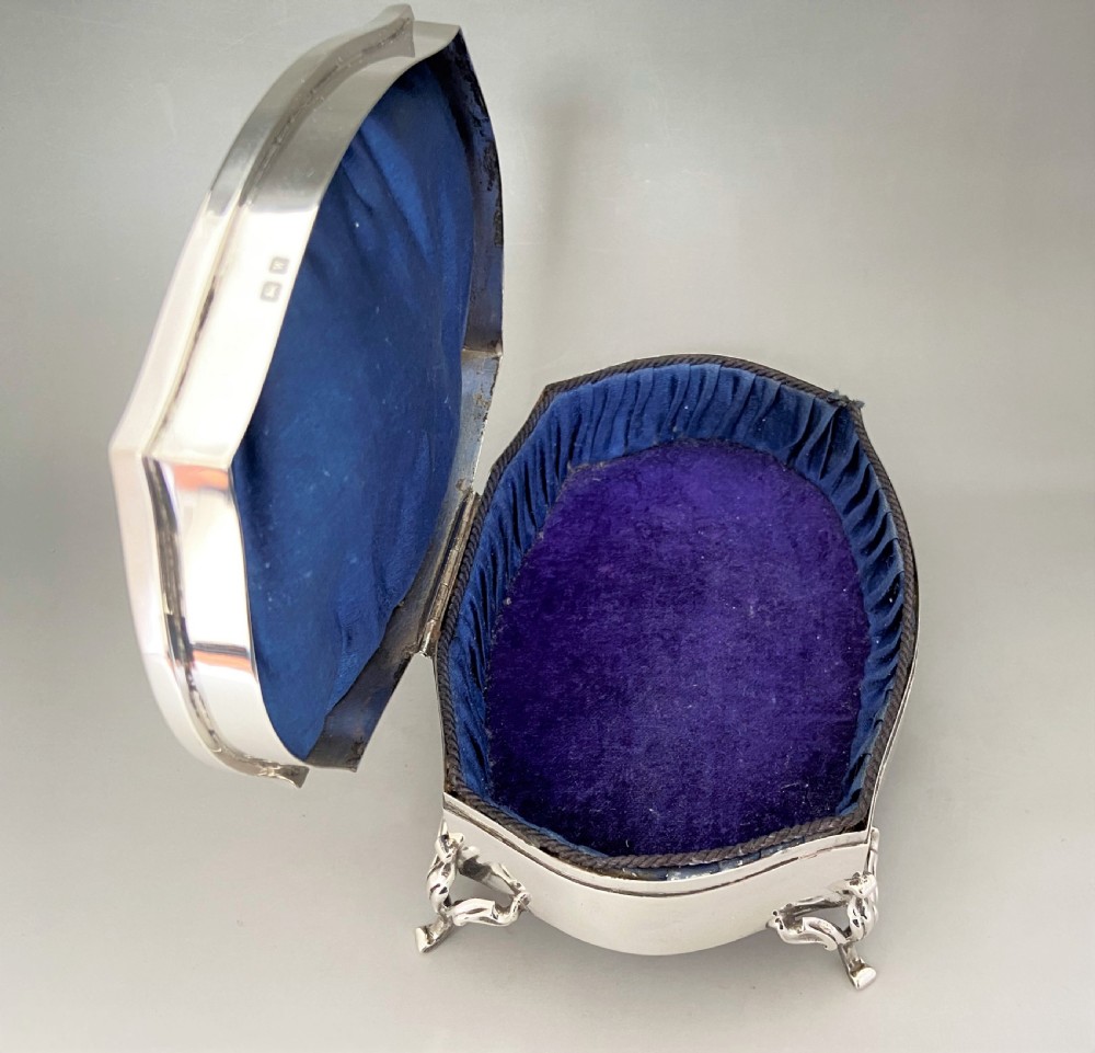 An octagonal silver trinket box with four cabriole legs, an engraved monogram on the top, and stamped hallmarks on the side. View V