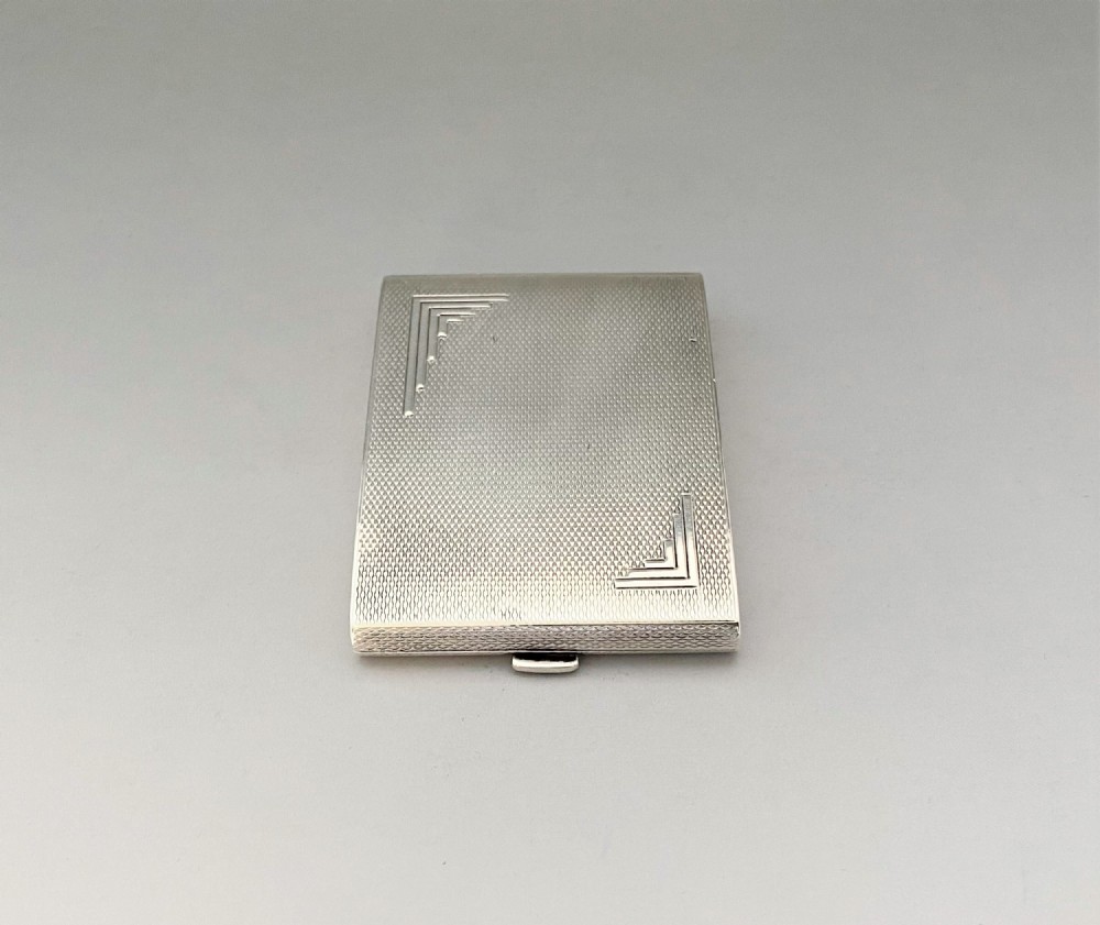 An Art Deco rectangular silver matchbook case featuring engine-turned crosshatch texturing and geometric stepped motifs in opposite corners.