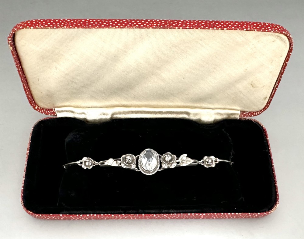 A mid-century silver bracelet featuring a central oval clear stone flanked by sculpted rose and leaf details.