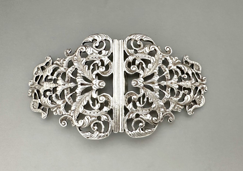 An ornate two-part cast silver buckle featuring intricate pierced foliate scrollwork and a central vertical connecting slot.
