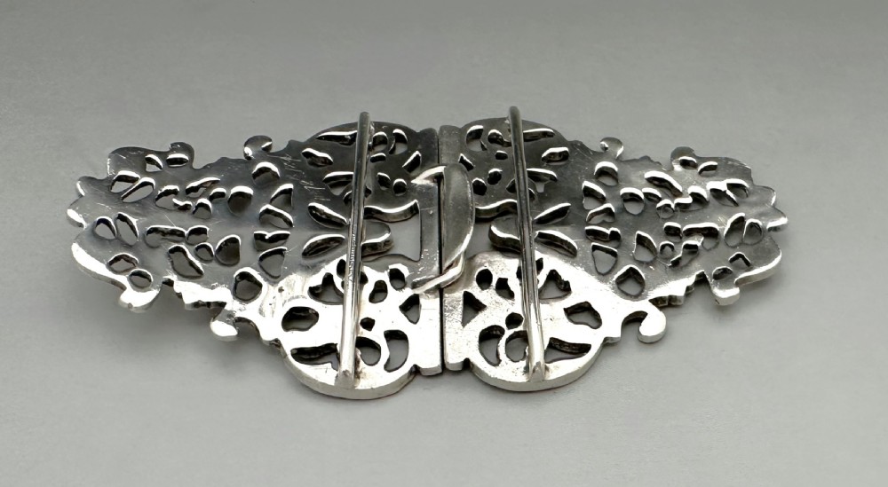 An ornate two-part cast silver buckle featuring intricate pierced foliate scrollwork and a central vertical connecting slot. View III