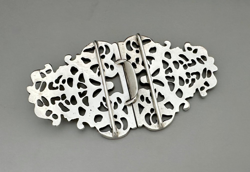 An ornate two-part cast silver buckle featuring intricate pierced foliate scrollwork and a central vertical connecting slot. View VI