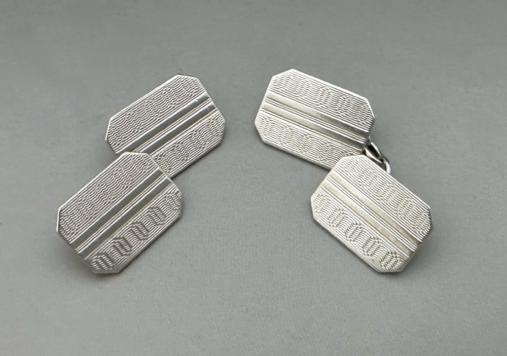 A pair of mid-20th-century silver double-sided cufflinks with engine-turned wavy patterns and octagonal faces connected by chain links.