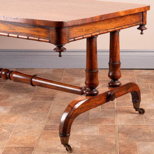 fig 1. A low 19th-century rectangular rosewood coffee table featuring twin turned pedestal supports, a central stretcher, and splayed legs on brass castors.