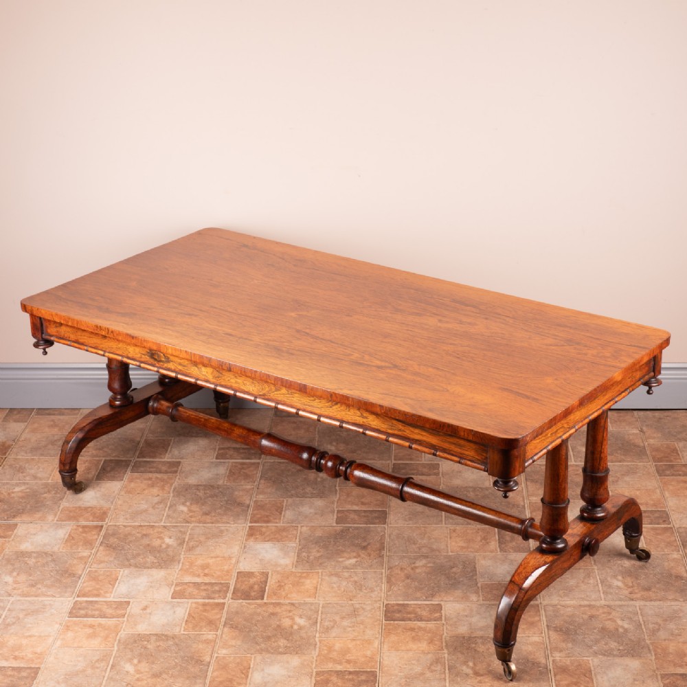 A low 19th-century rectangular rosewood coffee table featuring twin turned pedestal supports, a central stretcher, and splayed legs on brass castors.