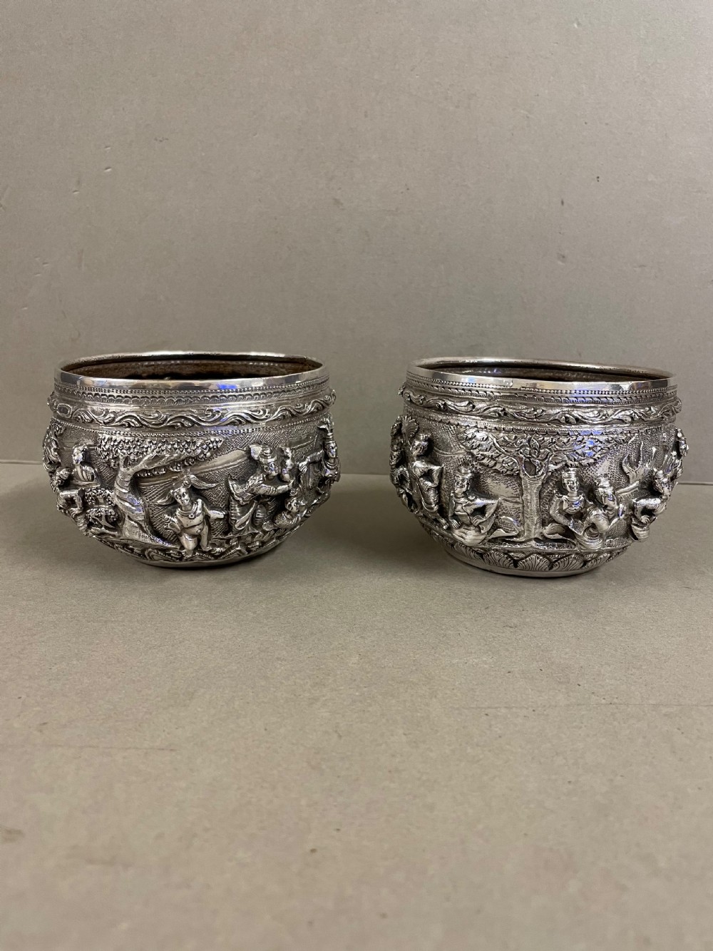 A pair of round antique Burmese silver bowls featuring dense, high-relief figural scenes and traditional chased ornamentation.