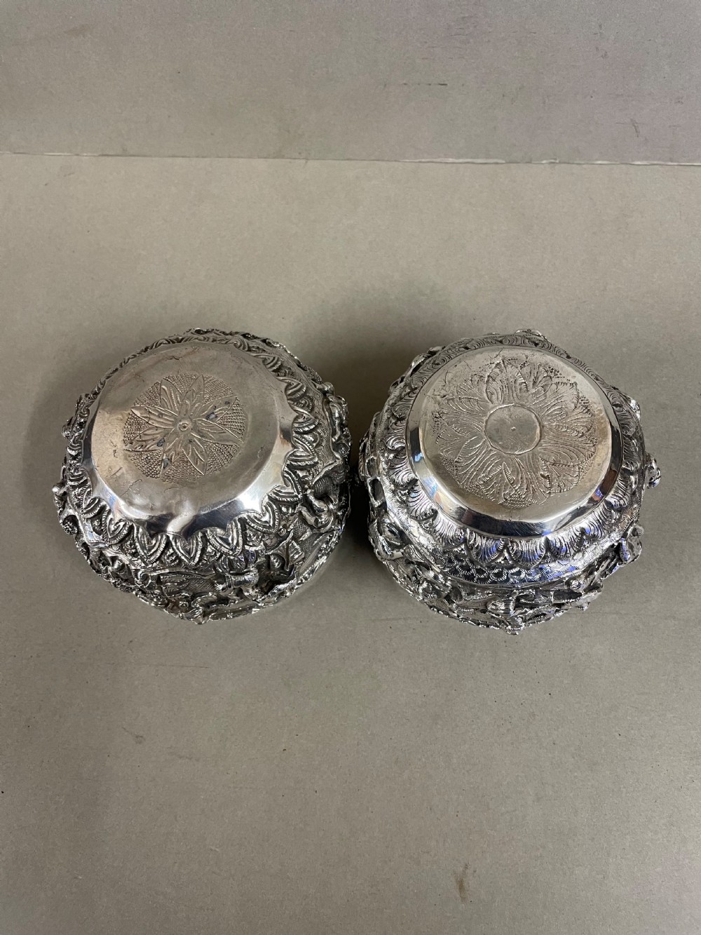 A pair of round antique Burmese silver bowls featuring dense, high-relief figural scenes and traditional chased ornamentation. View V