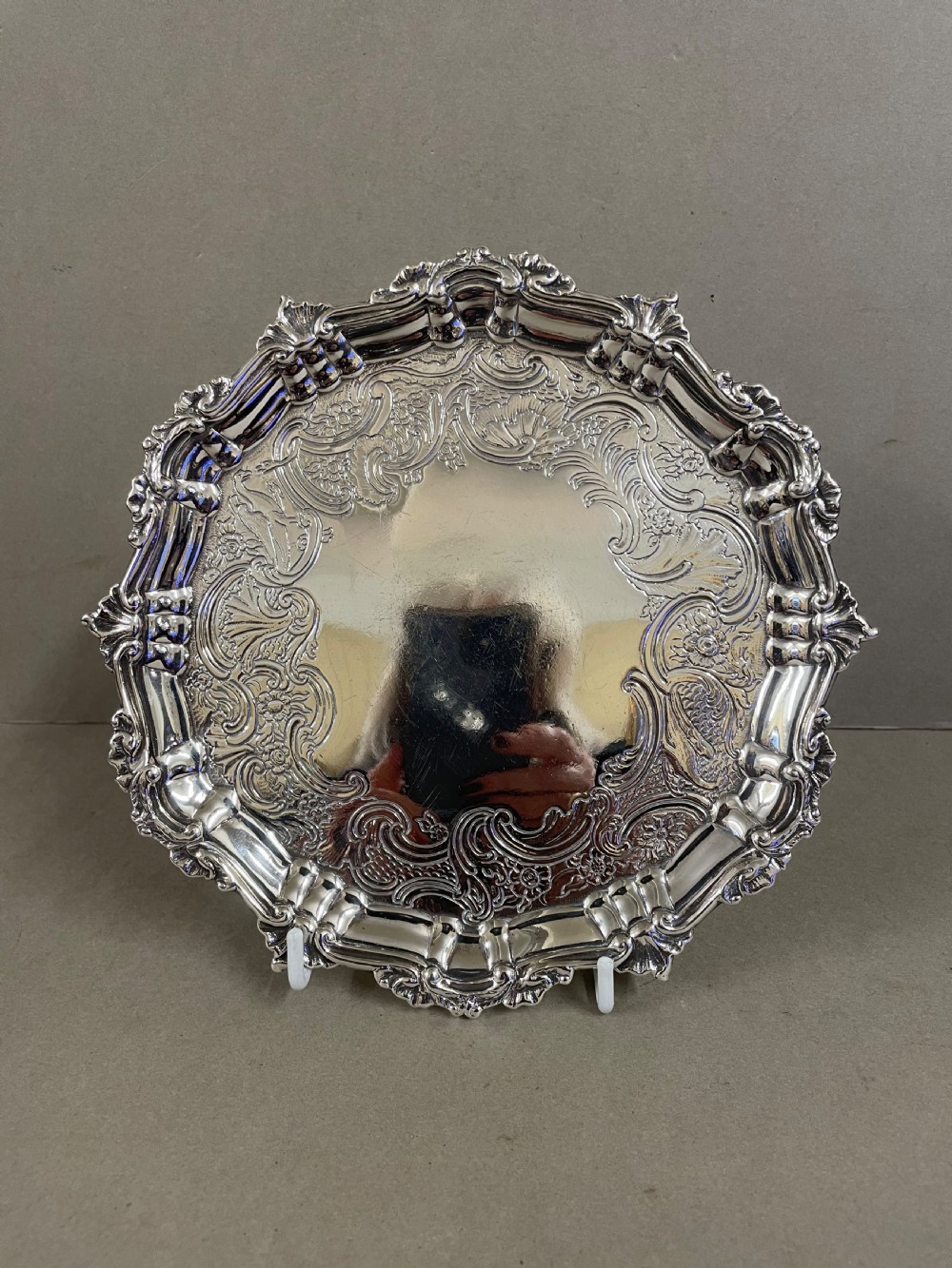An ornate circular antique silver salver featuring heavily chased floral scrollwork and a raised scalloped rim. View II