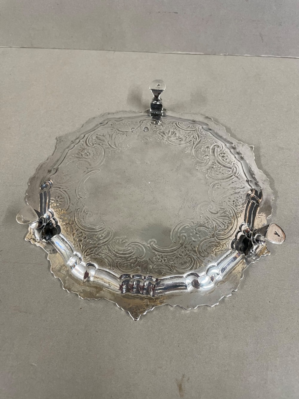 An ornate circular antique silver salver featuring heavily chased floral scrollwork and a raised scalloped rim. View III