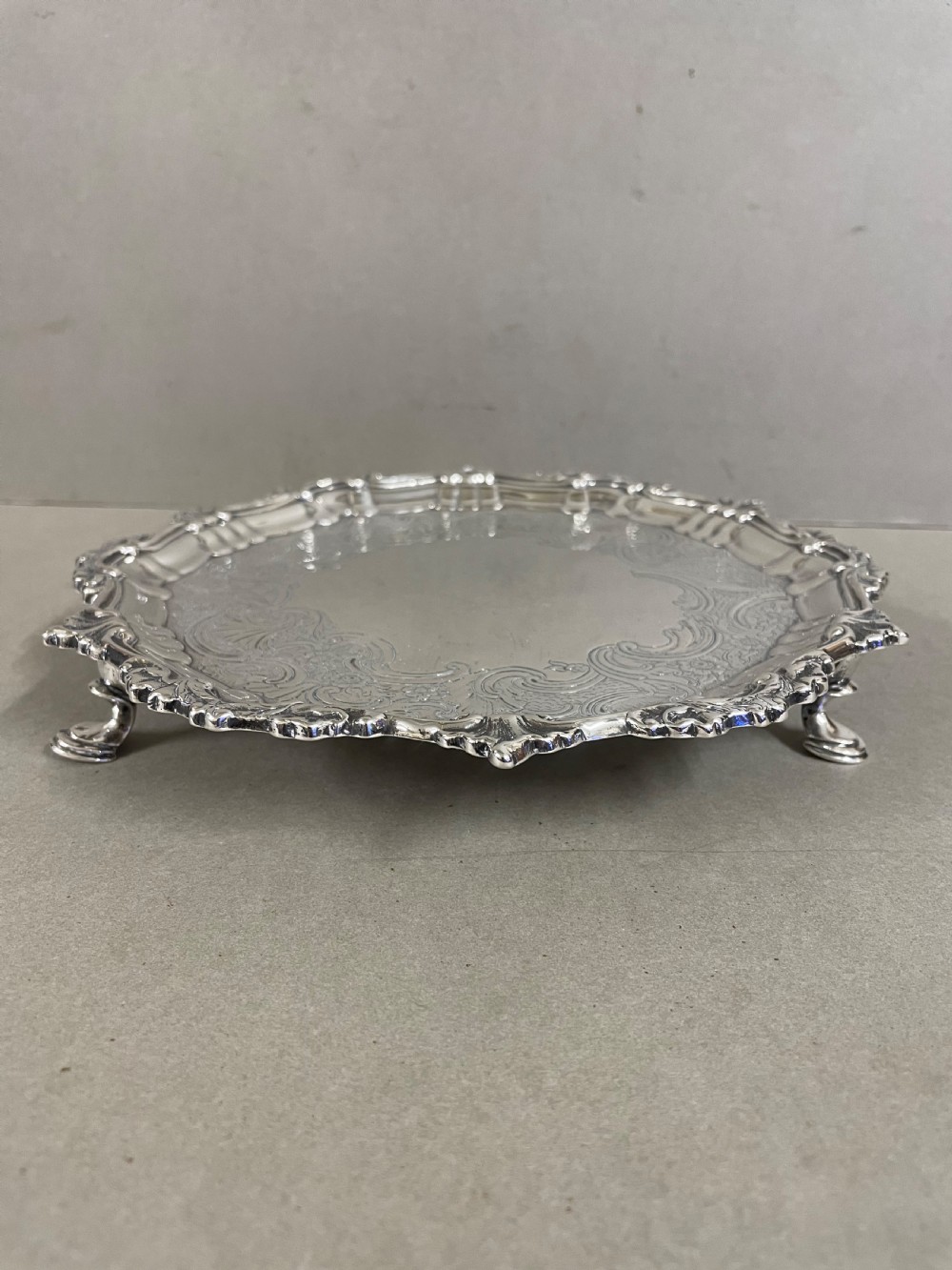An ornate circular antique silver salver featuring heavily chased floral scrollwork and a raised scalloped rim. View V
