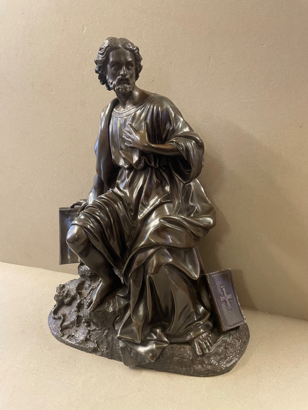 A dark bronze sculpture of a bearded male figure, identified as Saint Paul, kneeling amongst rocky terrain with books at his side. View II