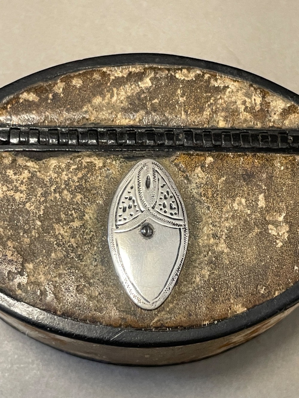 An oval antique snuff box featuring a mottled leather-covered body, a hinged lid, and an engraved metal escutcheon plate. View II