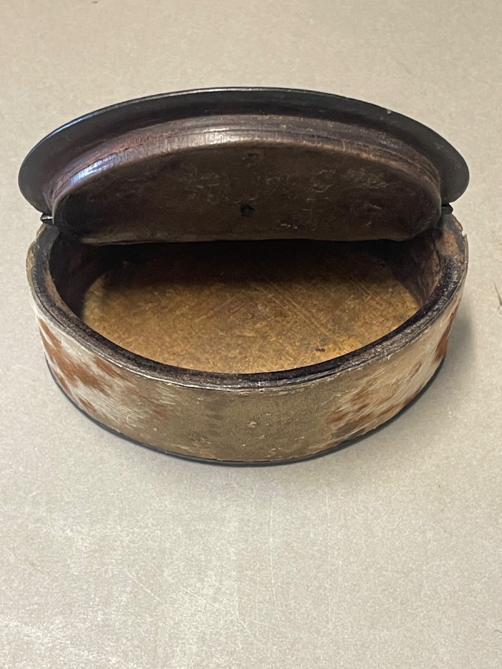 An oval antique snuff box featuring a mottled leather-covered body, a hinged lid, and an engraved metal escutcheon plate. View IV