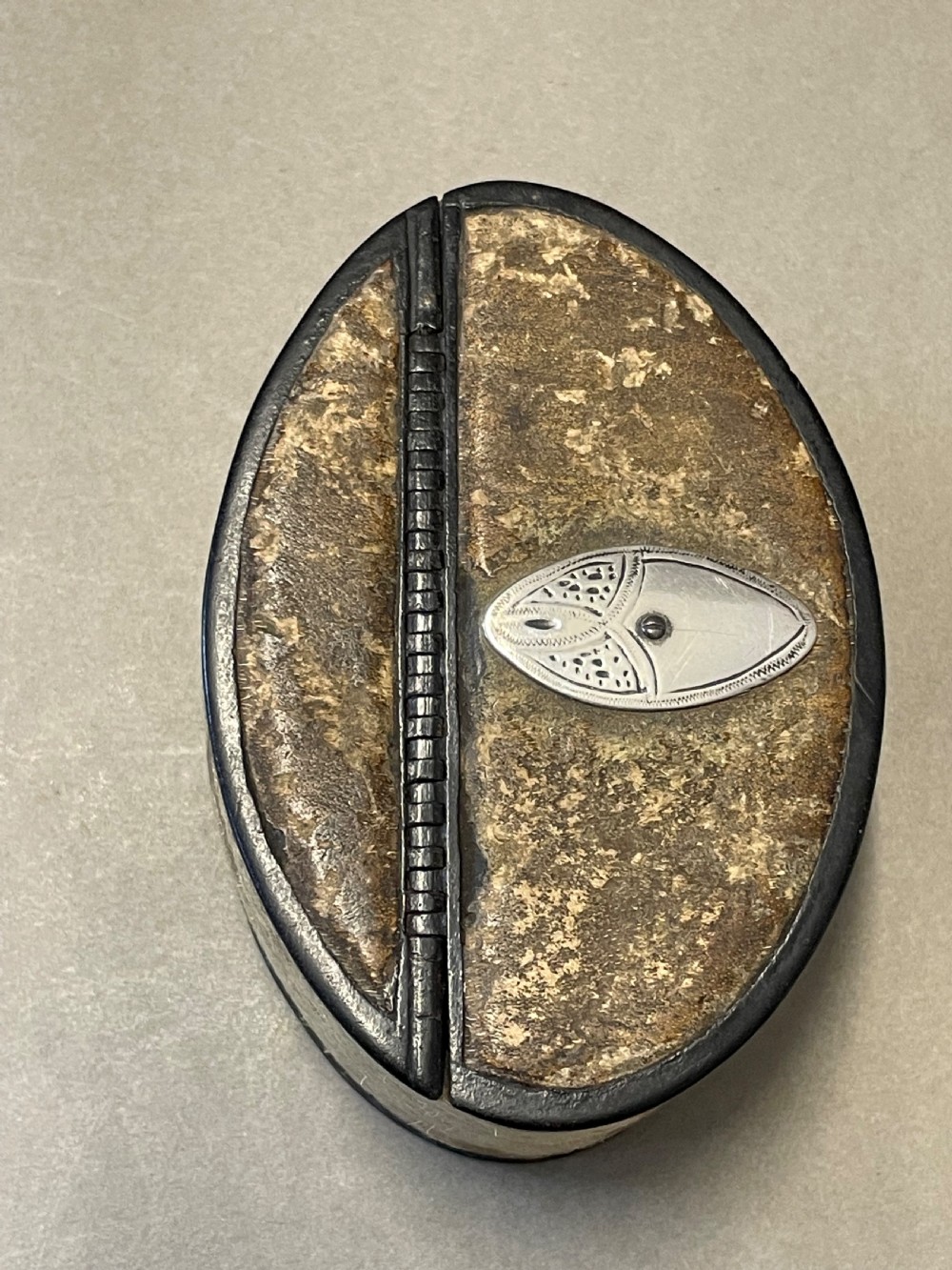 An oval antique snuff box featuring a mottled leather-covered body, a hinged lid, and an engraved metal escutcheon plate. View VII