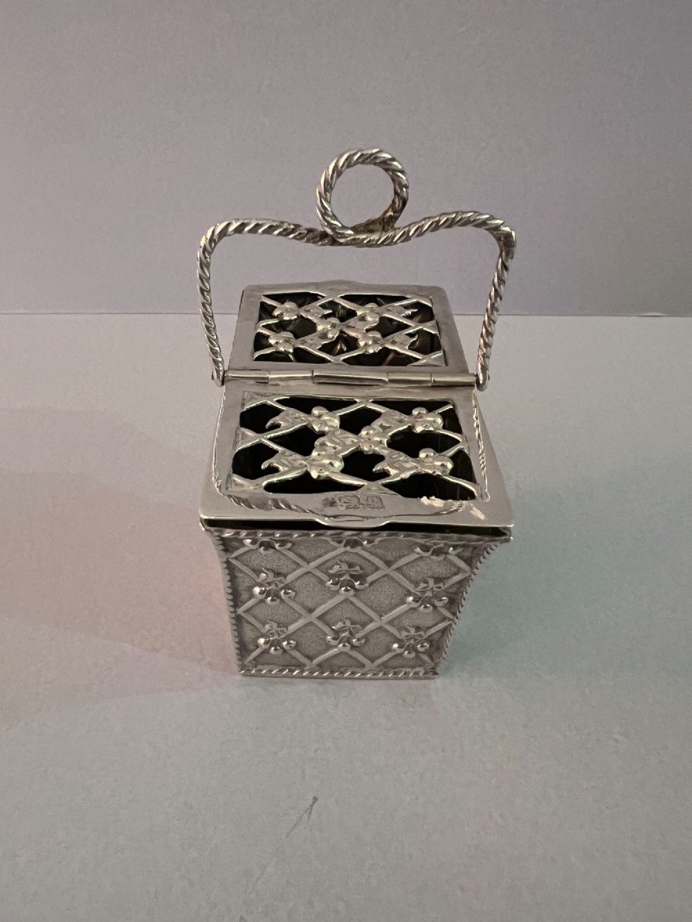 A small silver basket featuring double hinged pierced lids, a central rope-twist handle, and a diaper-patterned body with floral motifs. View II