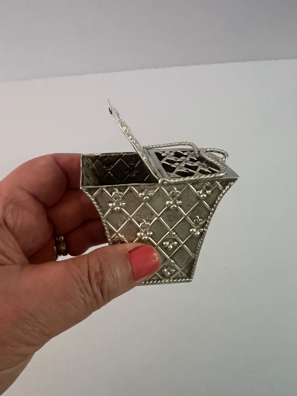 A small silver basket featuring double hinged pierced lids, a central rope-twist handle, and a diaper-patterned body with floral motifs. View III