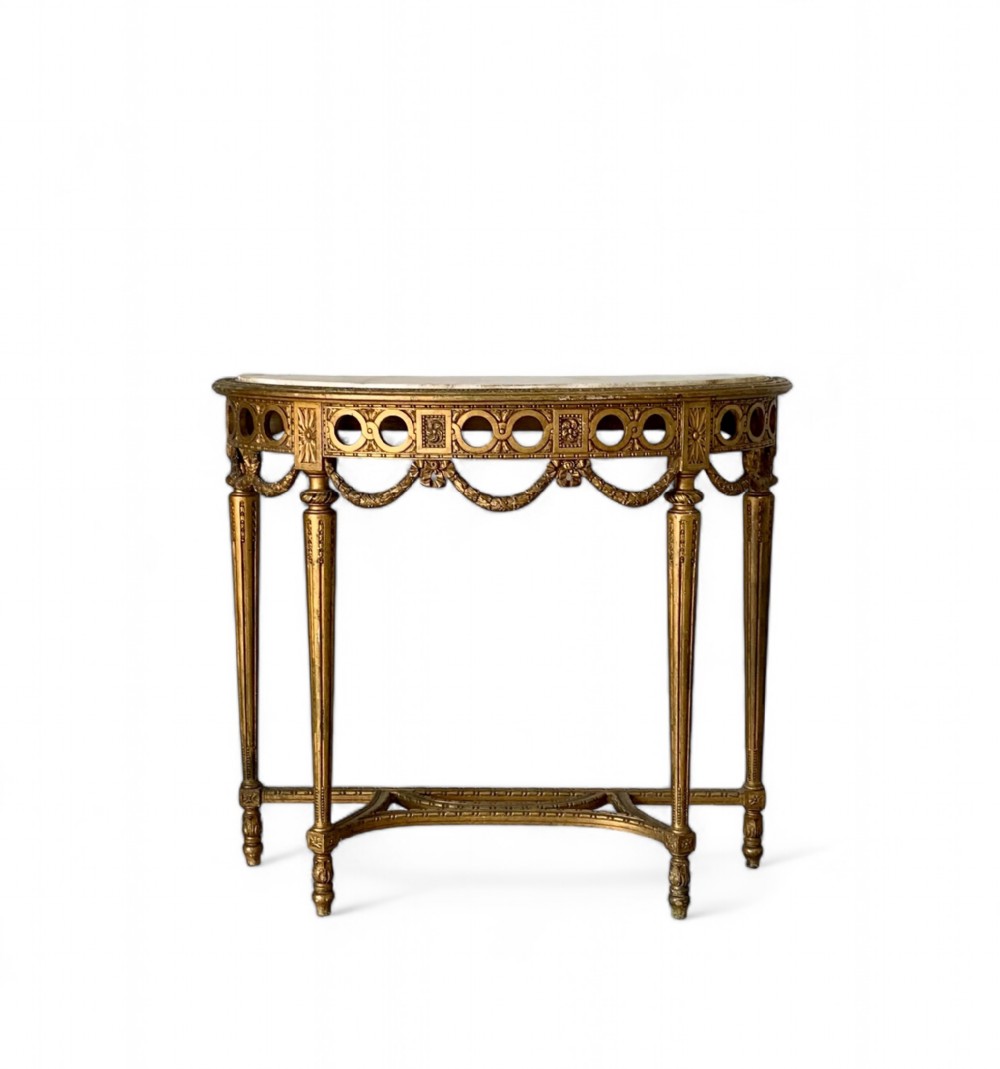 A French Louis XVI style giltwood console table featuring fluted tapered legs, carved garland swags, a pierced frieze, and a fitted marble top.