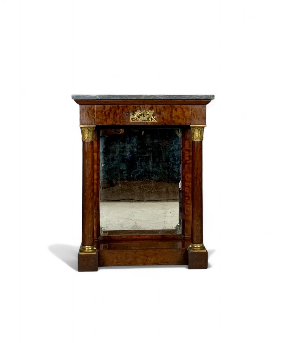 A French Empire mahogany console table featuring a grey marble top, gilt bronze column capitals, a central figural frieze mount, and a mirrored back plate.