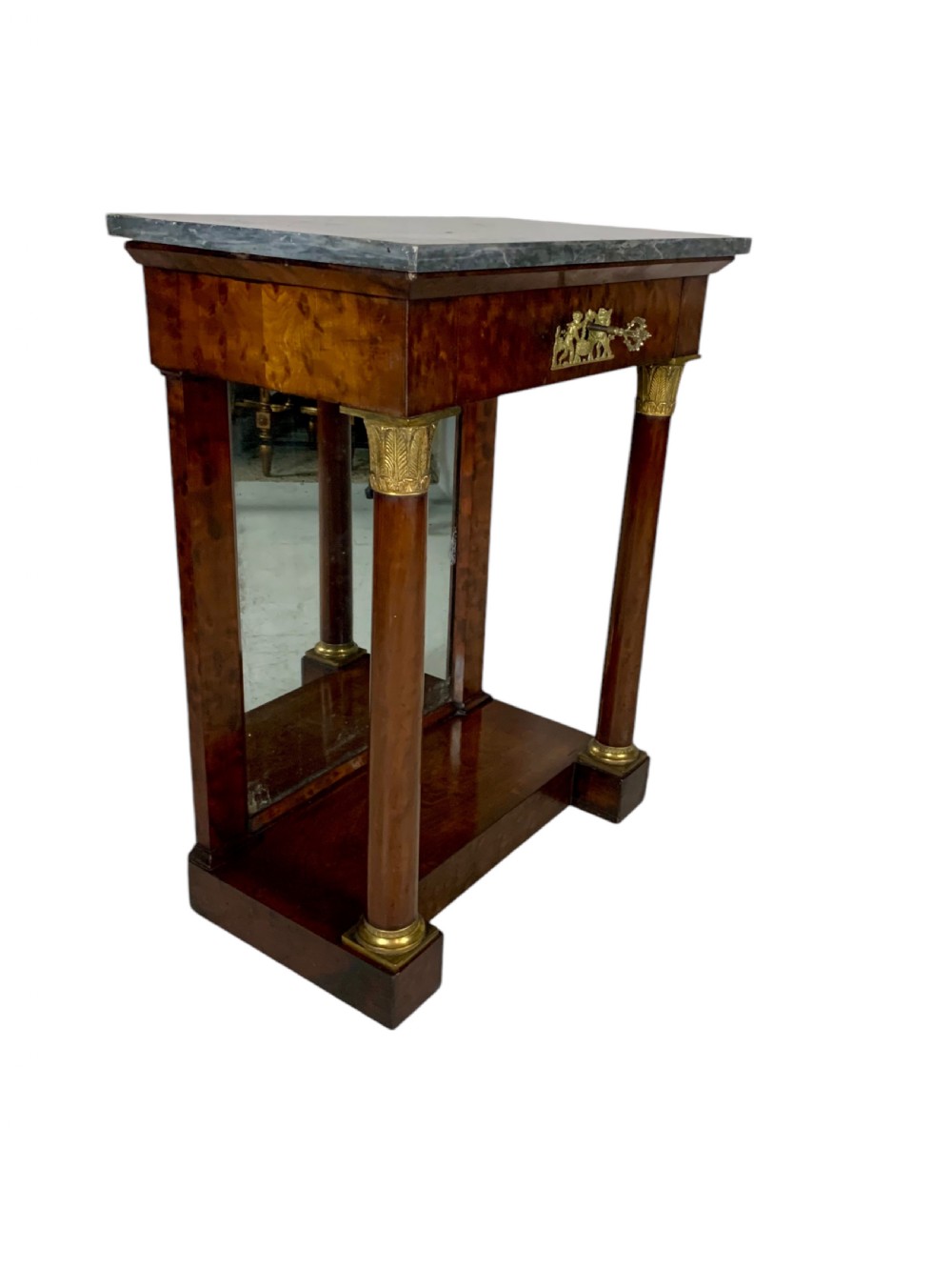 A French Empire mahogany console table featuring a grey marble top, gilt bronze column capitals, a central figural frieze mount, and a mirrored back plate. View VI