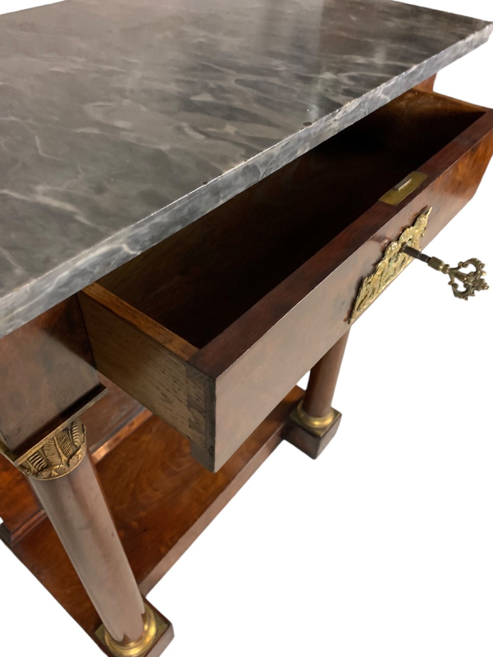 A French Empire mahogany console table featuring a grey marble top, gilt bronze column capitals, a central figural frieze mount, and a mirrored back plate. View VII