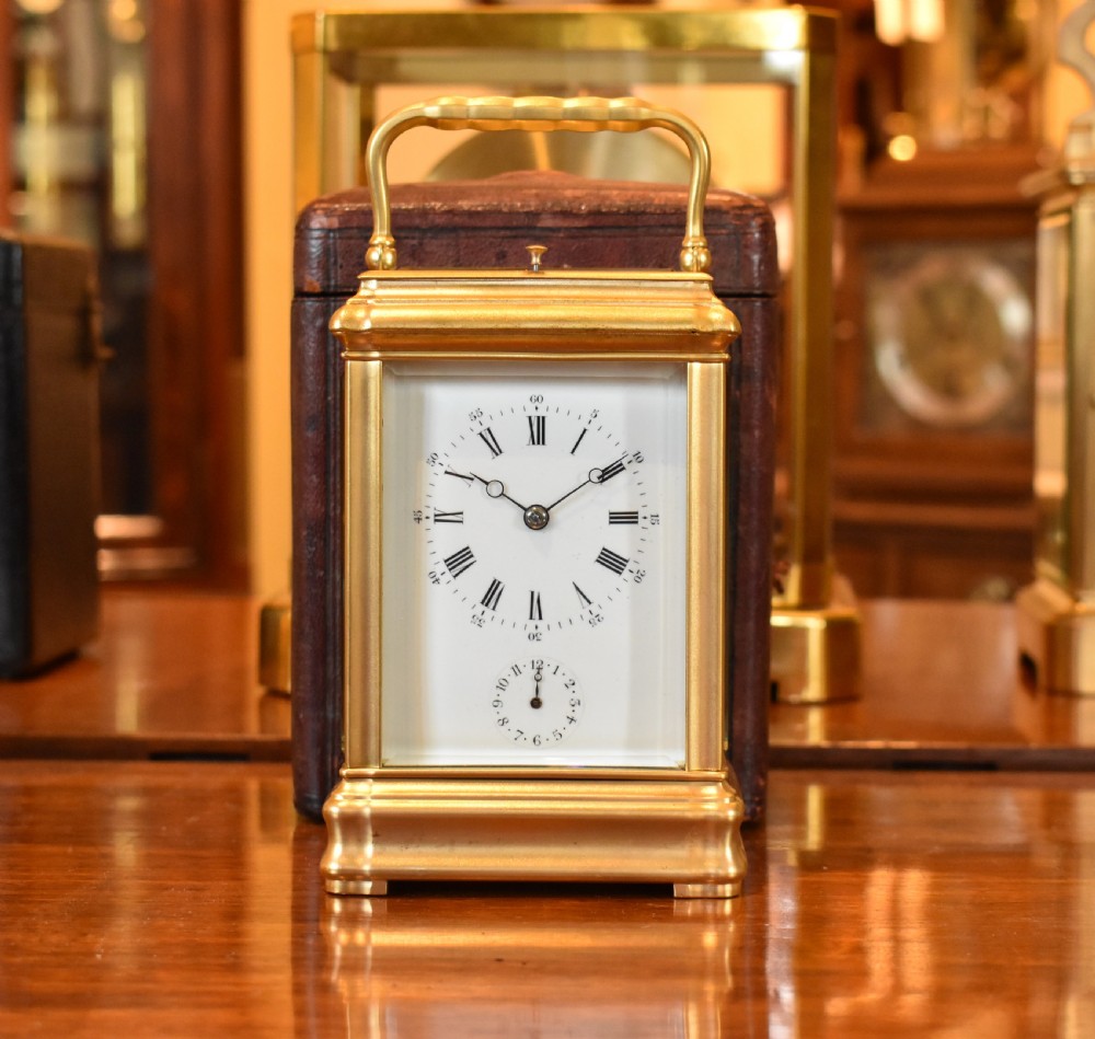 A French gilt brass carriage clock featuring a rectangular glass case, top carrying handle, and white enamel dial with Roman numerals.