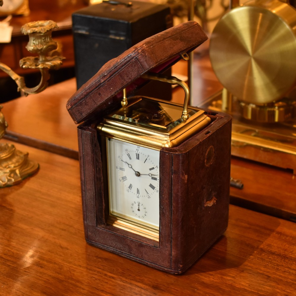 A French gilt brass carriage clock featuring a rectangular glass case, top carrying handle, and white enamel dial with Roman numerals. View V
