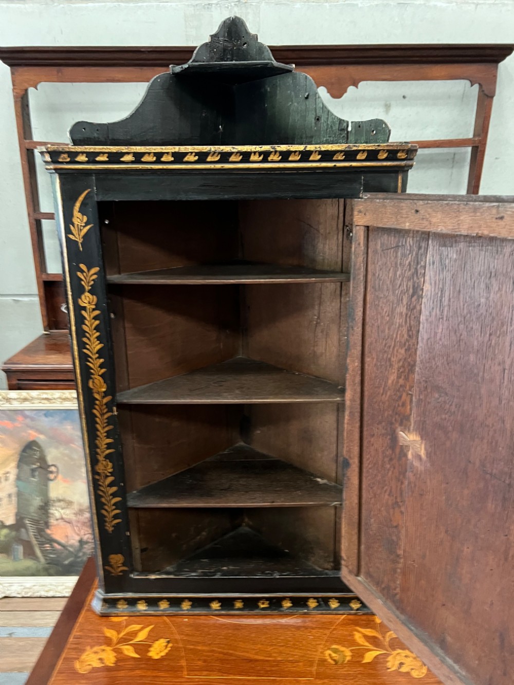 A dark black japanned hanging corner cabinet featuring gilt chinoiserie artwork with birds, architectural pagodas, and brass hinges. View II