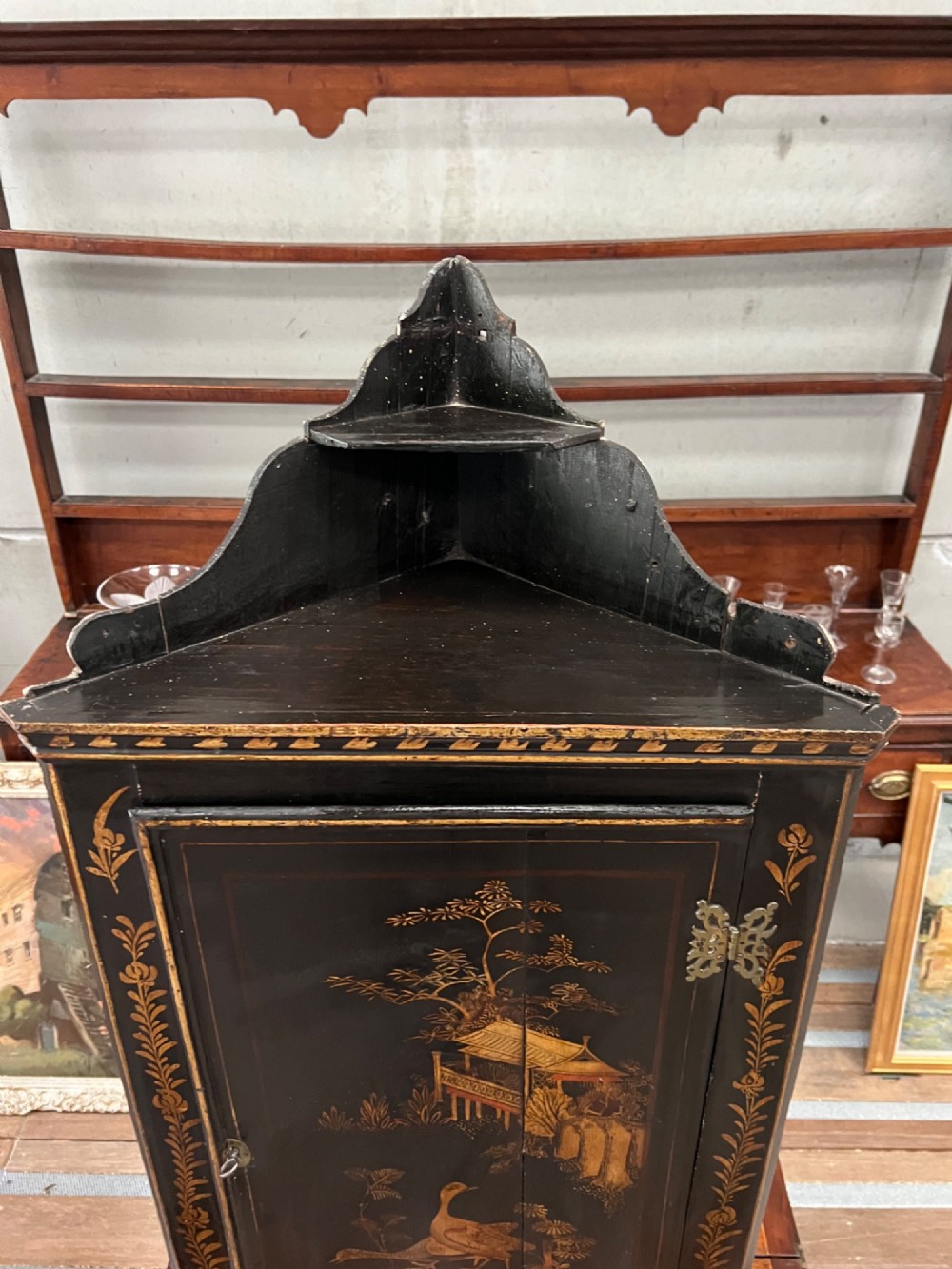 A dark black japanned hanging corner cabinet featuring gilt chinoiserie artwork with birds, architectural pagodas, and brass hinges. View III
