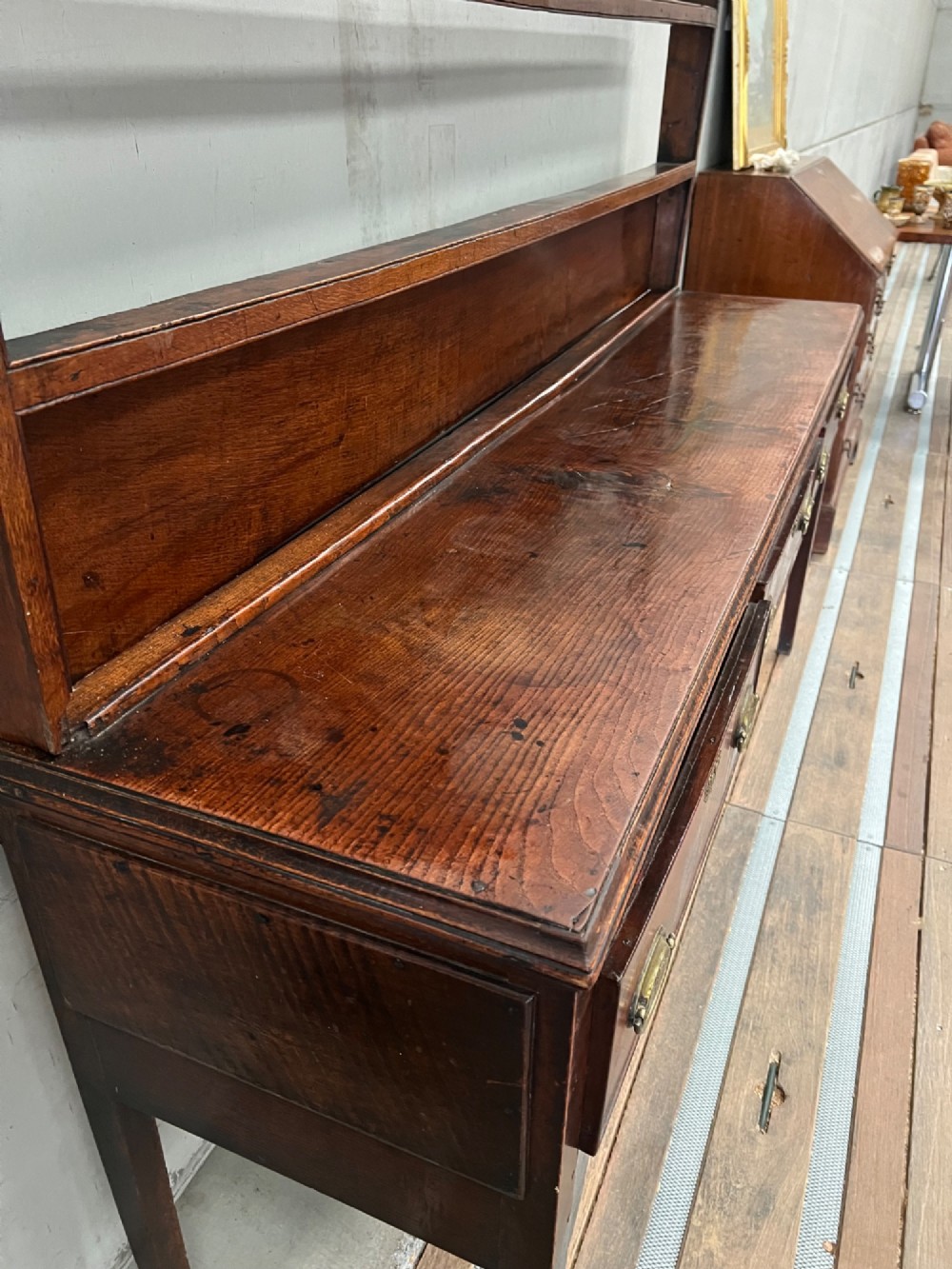 An 18th century oak and elm Welsh dresser featuring an open three-tiered plate rack top above three drawers with brass handles and a shaped apron. View II