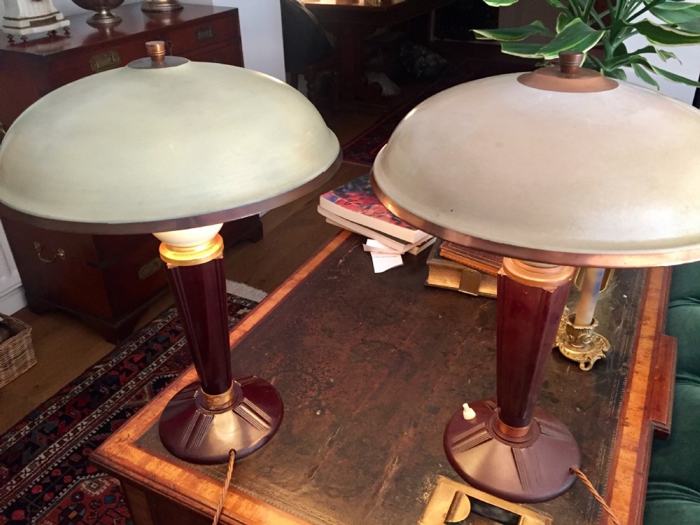 A near pair of Art Deco desk lamps featuring stepped dark brown Bakelite bases, fluted stems, and wide rounded metal shades with internal illuminated glass diffusers. View II