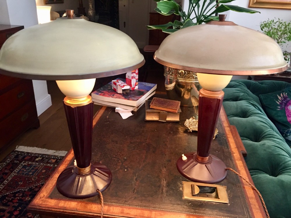 A near pair of Art Deco desk lamps featuring stepped dark brown Bakelite bases, fluted stems, and wide rounded metal shades with internal illuminated glass diffusers. View VIII