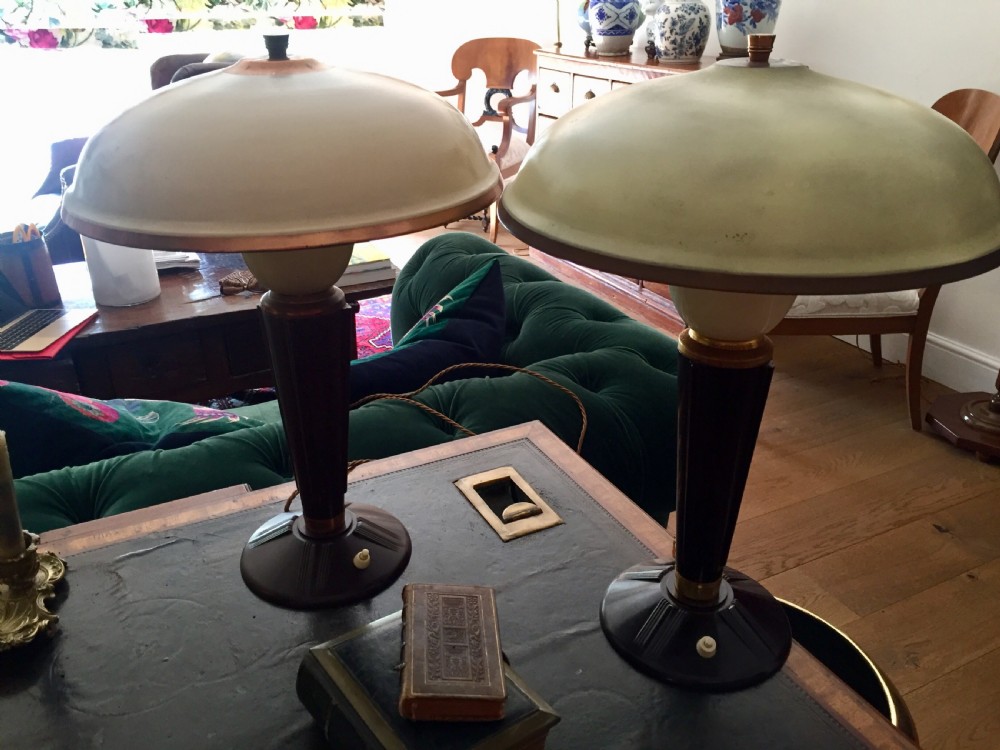 A near pair of Art Deco desk lamps featuring stepped dark brown Bakelite bases, fluted stems, and wide rounded metal shades with internal illuminated glass diffusers. View III