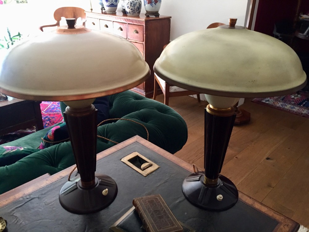 A near pair of Art Deco desk lamps featuring stepped dark brown Bakelite bases, fluted stems, and wide rounded metal shades with internal illuminated glass diffusers. View VI